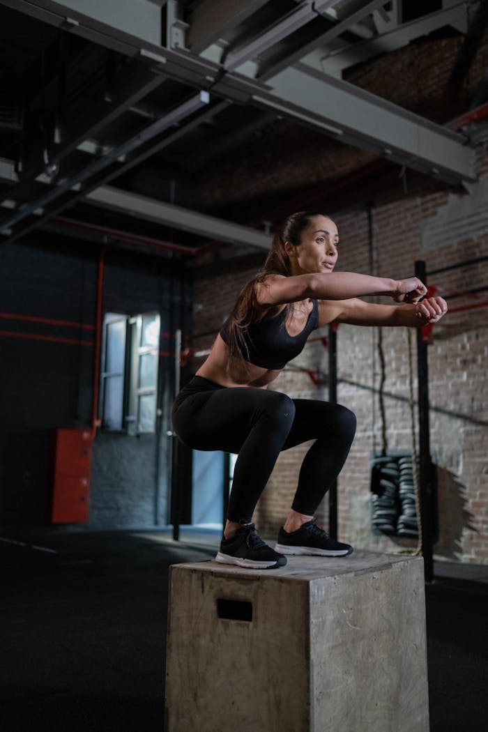 services-02 Fit woman in activewear executing a box jump inside a modern gym setting.