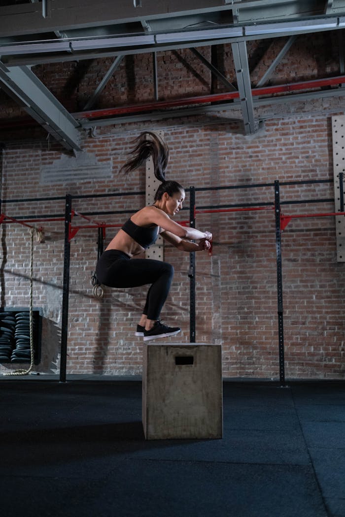 contact-img-02 A fit woman executes a box jump in a gym setting, showcasing athleticism and fitness.